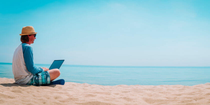 Een man met een laptop zit op het strand aan zee
