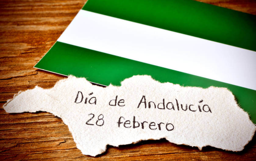Flagge von Andalusia mit einem Stück Papier - Día de Andalucía, 28 febrero - auf einem Holztisch