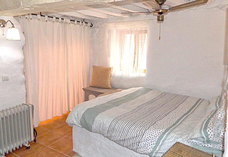 Guest bedroom with ceiling fan, typical andalusian village window and wardrobes.