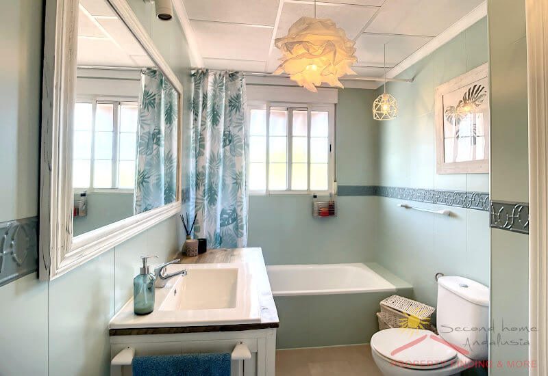 Großes Badezimmer mit Fenster, einer Badewanne, Toilette und Waschbecken mit grünen Fliesen