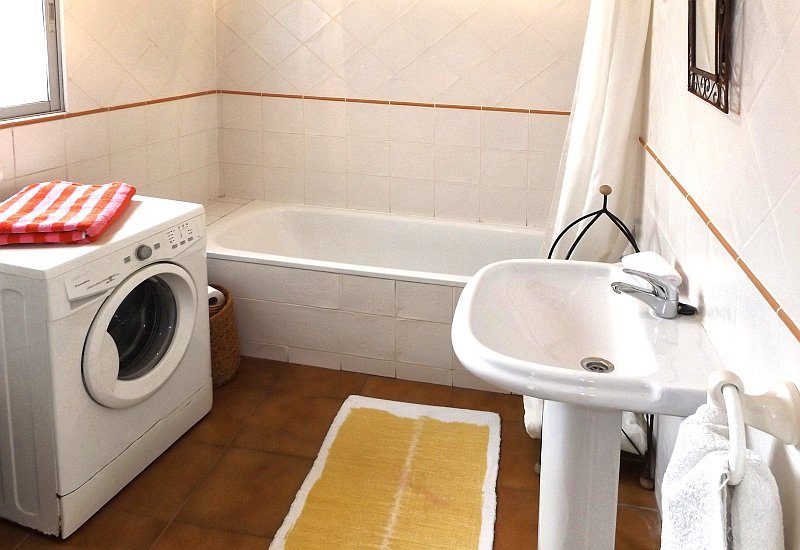 The bathroom is equipped with a toilet, a bath tube, basin and has space for a washing machine