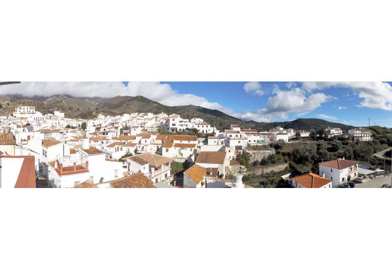 Gorgeous panoramic view of Sedella with mountains inwhite clouds and a blue sky.