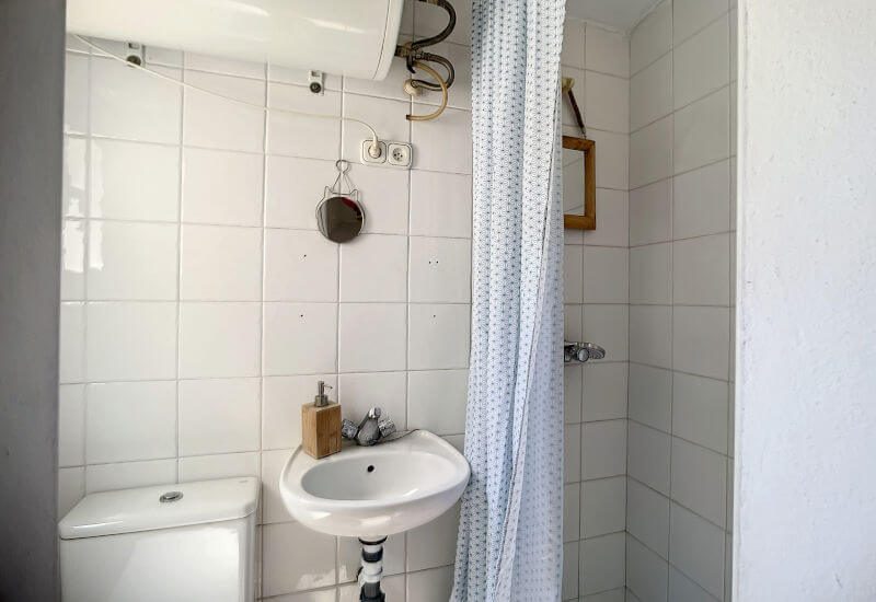Kleine badkamer met douche, wastafel en toilet. Licht door het raam.