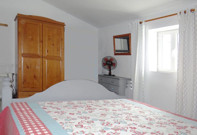 Schlafzimmer mit Doppelbett kleinem Fenster auf das Dorf und Wandschrank aus Holz
