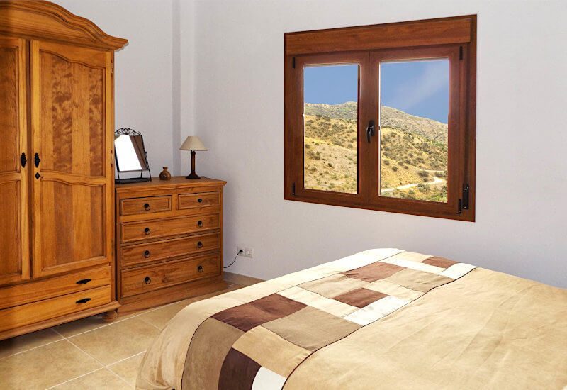 Slaapkamer 2 heeft een houten kledingkast en een raam met uitzicht op het landschap.