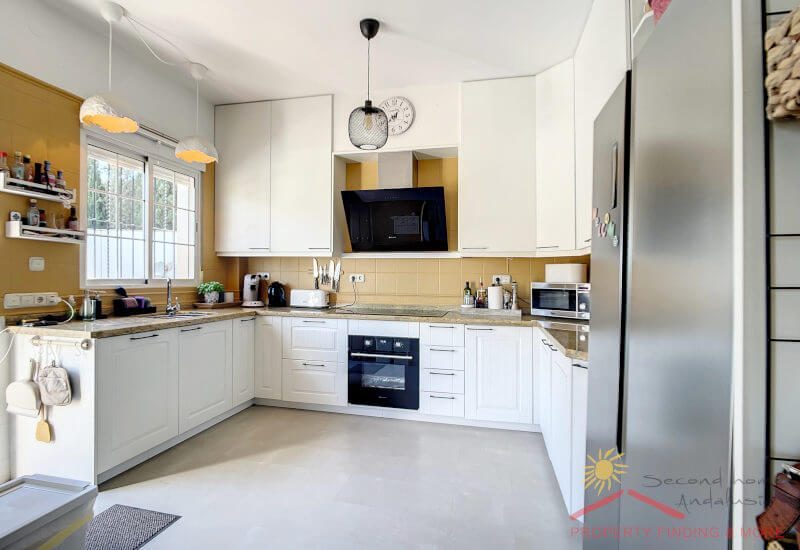 eine große, moderne, helle, weiße Küche mit einem Fenster und einer Tür zur Terrasse