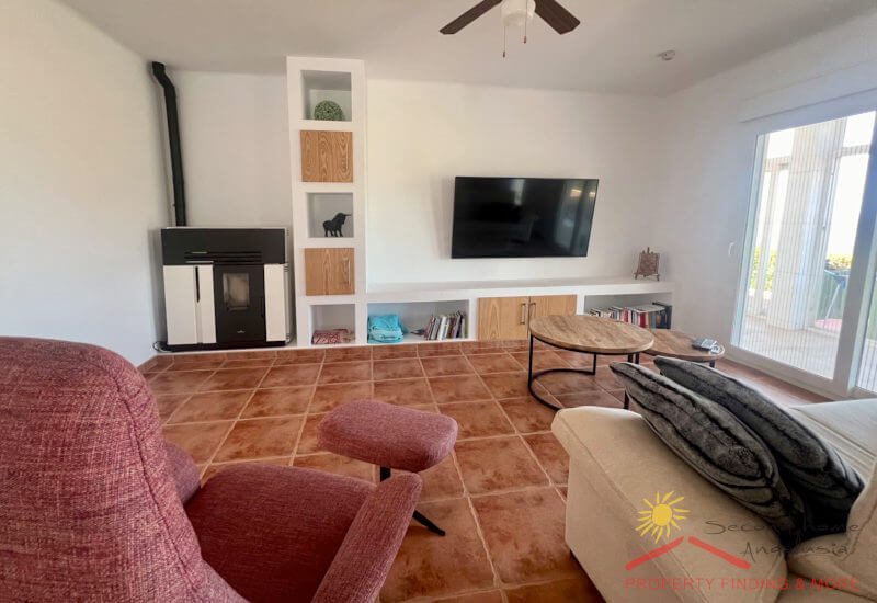 Living room with sofa and TV armchair, modern wood-burning stove and large TV
