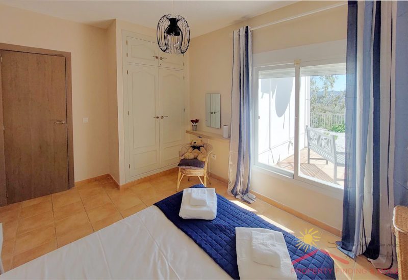 big bedroom with in-build white wooden wardrobe and big windows to the terrace