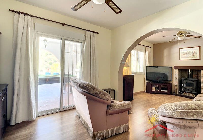 Der Salon hat ein großes Fenster und eine große Glastür zum Garten