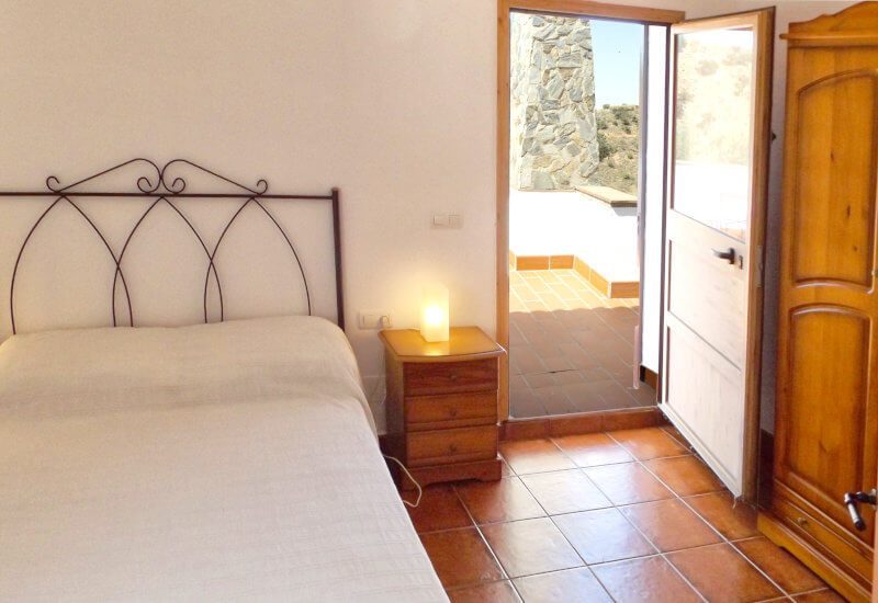 Guest room 1 has a queen size bed, a wooden wardrobe and a large door to the terrace.