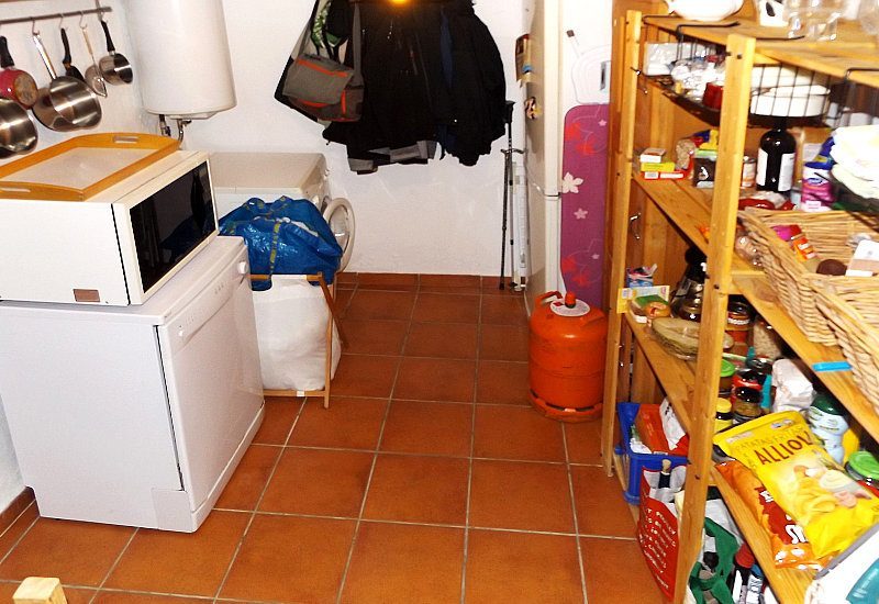 Pantry behind the kitchen with storage shelfs, washing machine, dish washer, microwave and fridge.