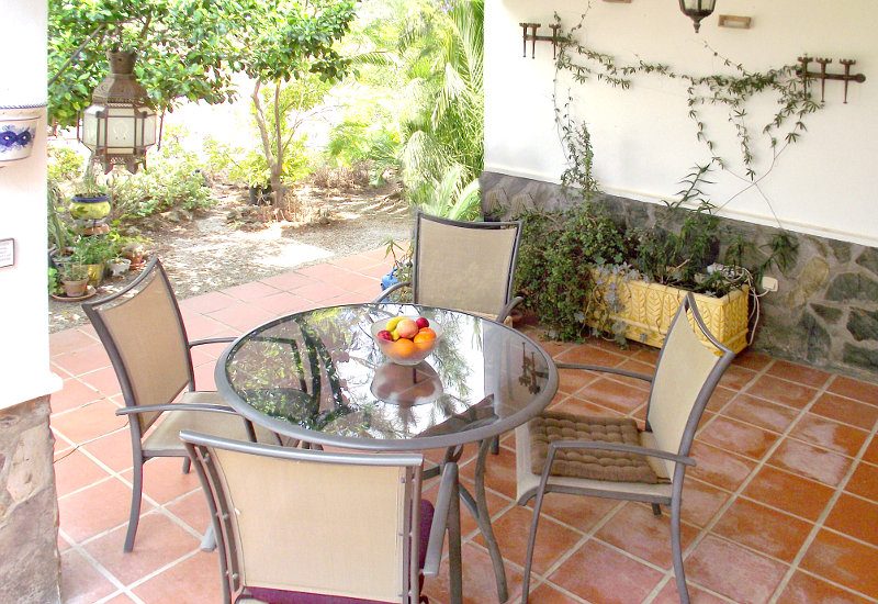 Overdekt terras met glazen tafel en moderne stoelen heeft uitzicht op de tuin