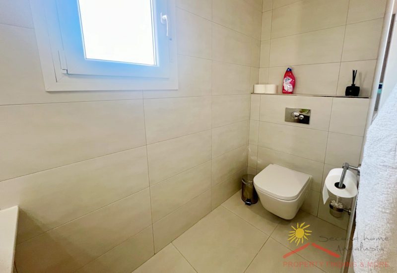 A separate toilet with a small window and washbasin